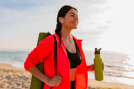 young-attractive-smiling-woman-doing-sports-morning-sunrise-sea-beach-holding-yoga-mat-bottle-water-healthy-lifestyle-listening-music-earphones-wearing-pink-windbreaker-jacket